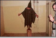 Abu Ghraib torture picture: A hooded man standing on a box with electrical wires attached to his hands and testes